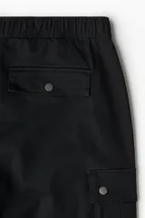 Pantalón cargo negro de corte holgado, con cintura elástica, bolsillos laterales, bolsillos tipo cargo con solapa y botón a presión en los laterales y bolsillos traseros con solapa y botón a presión.