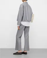 Chaqueta bomber gris con cuello italiano, cierre frontal con broches a presión y bajo abullonado. Las mangas son redondeadas con pinzas en los codos y cuenta con bolsillos verticales en las costuras laterales.