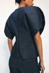 Blusa de Zara confeccionada en mezcla de algodón con acabado denim. Presenta escote redondo, mangas cortas abullonadas con volumen y costuras con pespuntes a contraste. Cierre posterior con cremallera oculta.