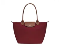 Bolso tipo tote bag de nylon color borgoña, con asas y solapa de cuero marrón. Presenta cierre superior y herrajes dorados.