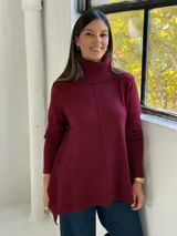Sweater de punto color bordó con cuello alto tipo polera, diseño de corte evasé con costura central vertical y bajo asimétrico más largo en la parte posterior.