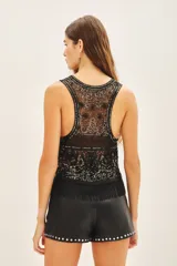 Top corto sin mangas con escote redondo, confeccionado en tul bordado con lentejuelas, piedras y canutillos. Presenta un diseño con flecos de mostacillas en el ruedo y una tira larga decorativa al cuello.