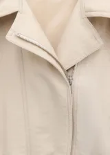Chaqueta oversize color crudo, con cuello alto, cierre frontal con cremallera, panel fruncido en la cintura, mangas largas y bolsillos laterales.
