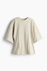 Top de punto fino color beige, de corte holgado con cuello redondo, hombros caídos y mangas al codo. Presenta costuras decorativas frontales y bajo levemente acampanado.