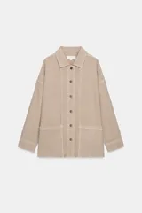 Sobrecamisa de mujer color beige claro, con cuello solapa, manga larga y bolsillos de plastrón en el delantero. Presenta bajo asimétrico con aberturas laterales y cierre frontal de botones.