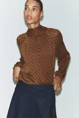 Blusa de cuello subido con diseño de lunares, manga larga abullonada con puños elásticos y forro interior.