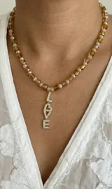 Collar corto de cuentas de cristal facetado en tonos ámbar y perlas, con un dije colgante dorado que forma la palabra 'LOVE' decorado con circonias brillantes.