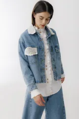 Campera de jean azul con detalles de tejido crochet en color blanco en el cuello y en uno de los bolsillos frontales. Posee cierre frontal con botones metálicos y un corte clásico.