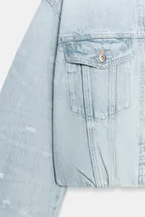 Campera de jean crop color celeste con efecto lavado, cuello solapa, mangas largas con hombreras, bolsillos con solapa en el pecho y detalles de rotos. Cuenta con cierre frontal de botones y bajo fruncido.