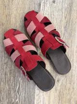 Suecos tipo sandalias franciscanas elaborados en cuero, con tiras entrelazadas de gamuza en tonos rojo, rosado y bordó. Cuentan con una hebilla metálica lateral y suela plana.