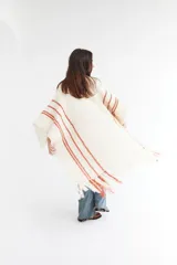 Ruana artesanal color crudo con rayas horizontales color ladrillo y flecos.