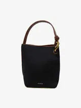 Bolso de hombro negro tipo bucket con asa de cuero marrón, logo de JW Anderson y cierre magnético.