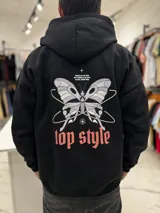 Canguro oversize negro con capucha y bolsillo tipo canguro. En la espalda presenta una estampa grande con diseño de mariposa, texto y la inscripción "top style" en color coral.