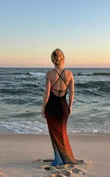 Vestido largo de seda o material similar, con tirantes finos y escote drapeado tipo cowl neck. Presenta un efecto degradado de color que va del negro/marrón oscuro en el busto, pasando por tonos naranjas y amarillos, hasta terminar en un azul vibrante en el ruedo.