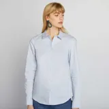 Camisa de corte ajustado en color azul claro, con cuello italiano, cierre frontal de botones y mangas largas con puños abotonados.