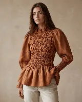 Blusa de algodón color tostado, con cuerpo elastizado tipo nido de abeja, mangas abullonadas con puños fruncidos, cuello alto con volado y dobladillo acampanado.