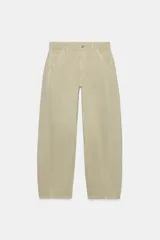 Jeans de tiro medio, estilo barrel, color beige con efecto desgastado. Presenta trabillas para cinto, bolsillos delanteros y traseros, y costuras decorativas curvadas a lo largo de las piernas.