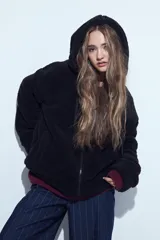 Canguro de corderito con capucha, cierre frontal y bolsillos laterales. Diseño relajado y textura suave.