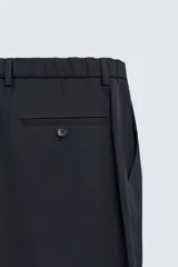 Pantalón de vestir regular fit color negro, confeccionado en tejido con mezcla de lana y elasticidad. Cuenta con cintura elástica, bolsillos frontales, bolsillos traseros de vivo con botón, y cierre frontal con cremallera y botón.