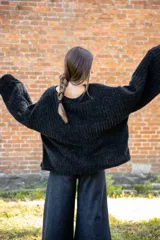 Buzo de textura tipo peluche en color negro, con diseño oversize, cuello amplio y mangas largas acampanadas.