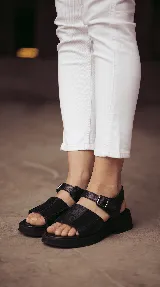Sandalia de cuero color negro con combinación de texturas, base de goma liviana, diseño chunky, tiras anchas en el empeine y tira con hebilla ajustable en el tobillo.