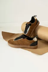 Championes urbanos de gamuza color marrón, con detalles en charol negro y bordes dorados. Presentan cordones negros y suela de goma al tono.