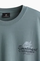 Remera de algodón verde militar, de corte holgado, con cuello redondo y mangas cortas. Cuenta con un pequeño estampado gráfico con texto en el pecho.