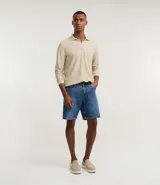 Bermuda de hombre confeccionada en denim de algodón, color azul medio, con tiro medio y corte recto. Presenta cierre de botón y cremallera, bolsillos delanteros y traseros, y etiqueta aplicada en la parte trasera de la cintura.