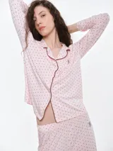 Camisa de pijama de manga larga con cuello solapa y cierre frontal de botones. Presenta un estampado sutil de pequeños corazones sobre una base de color gris melange, con detalles de ribete en contraste en el cuello y la botonera.