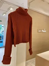 Sweater corto color ladrillo, de tejido de punto acanalado, con cuello alto y mangas largas con puños anchos.