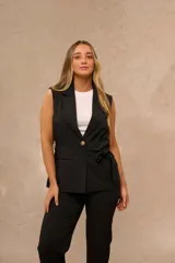 Chaleco sastrero largo color negro, con solapa clásica, cierre frontal con un botón y cinto ajustable del mismo género. Cuenta con dos bolsillos frontales con solapa.