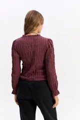 Blusa negra de algodón con textura fruncida en todo el cuerpo, cuello alto y puños con volados.