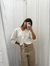 Blusa negra de lino con acabado brillante, de manga larga abullonada, escote con volados y cierre frontal con tiras para anudar.