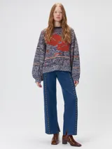 Sweater de punto con diseño geométrico y gráfico frontal en color rojo. Presenta cuello redondo, mangas largas holgadas y un ajuste suelto.