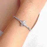 Pulsera de plata con diseño de cadena tipo tenis, adornada con un dije central en forma de flor de cuatro pétalos engastado con piedras brillantes.