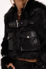 Campera de pelo sintético negro con detalles en cuero sintético, bolsillos frontales con solapa y cinturón ajustable con hebilla metálica.