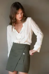 Falda corta color verde militar, estilo wrap o cruzada, con un bolsillo tipo parche con fuelle y un botón decorativo en el frente.