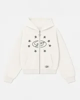 Buzo con cierre frontal, color crema, con diseño estampado de estrellas y logo en el pecho. Cuenta con capucha, bolsillos tipo canguro y tirador de cierre en forma de estrella.