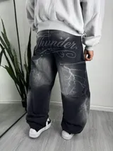 Jeans baggy negro de corte ancho, con efecto deslavado y estampado de rayos en los bolsillos traseros, además de la inscripción 'Thunder' en la parte superior.