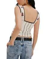 Top de punto color crema, ajustado al cuerpo, sin mangas y con escote cuadrado. Presenta bordados de rosas rojas y detalles de costura y ribetes en negro. Tiene cierre frontal con botones pequeños.