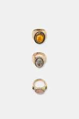Pack de tres anillos metálicos en tono dorado envejecido, cada uno con una piedra central de forma ovalada en colores amarillo, gris y rosa, con detalles labrados y texturizados en el metal.