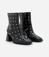 Bota de caña corta confeccionada en poliuretano color negro, con punta cuadrada, taco bloque y aplicación de studs metálicos en toda la superficie. Cuenta con cierre lateral.