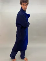 Tapado oversize desestructurado de lana merino afieltrada, teñido en degradé azul y negro. Tiene bolsillos laterales, cierre con broches ocultos y puños amplios que cubren la mano.