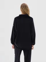 Camisa de terciopelo color negro, con cuello clásico, cierre frontal oculto y mangas largas con puños elásticos. Presenta un diseño holgado con cordón ajustable en el ruedo.