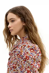 Camisa de popelina 100% algodón con estampado floral multicolor en tonos rojos, azules y amarillos sobre fondo blanco. Presenta cuello clásico camisero, hombros abullonados, mangas largas y botones de nácar en el frente.