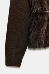 Chaqueta de punto gris con frente de piel sintética, cuello redondo, manga larga y cinturón fino efecto piel incorporado en la cintura. Cuenta con cierre frontal mediante ganchos metálicos y forro interior.