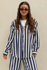 Camisa oversize a rayas verticales azules y blancas, de manga larga con puños abotonados y cierre frontal con botones blancos.