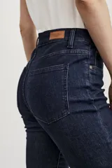 Pantalón de jean azul oscuro, de tiro medio, corte ajustado en las piernas y acampanado desde la rodilla hasta el tobillo. El ruedo es desflecado.