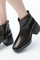Botas de caña baja color marrón oscuro, con punta cuadrada y plataforma con taco geométrico. Presenta cierre lateral y detalle de cuero con textura de cocodrilo en el talón.