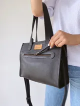 Cartera tipo tote bag de cuero color negro, con doble asa corta de mano y correa larga regulable y extraíble para usar al hombro o cruzada. Tiene un bolsillo frontal con cierre y un bolsillo interno.